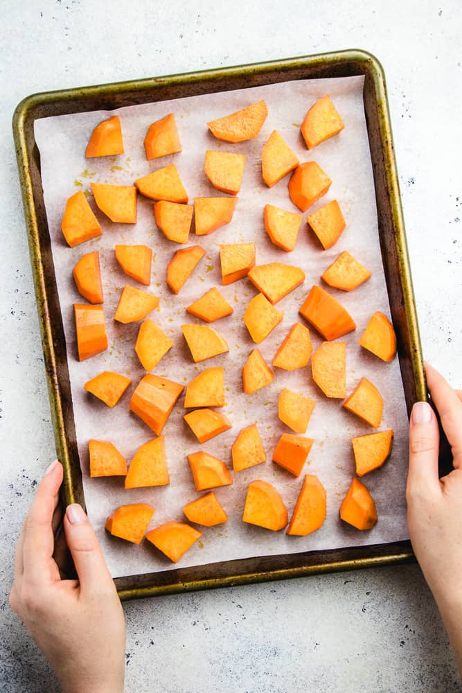 hands holding a baking sheet with dices sweet potato in it.