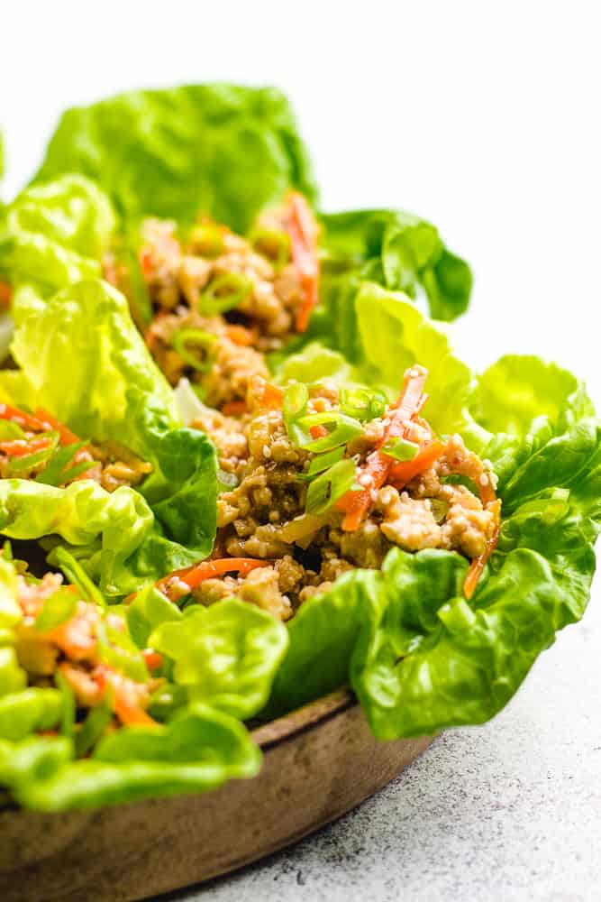 A close up photo of chicken lettuce wraps on a wooden plate.