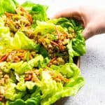a hand is grabbing a lettuce wrap from a wooden plate.