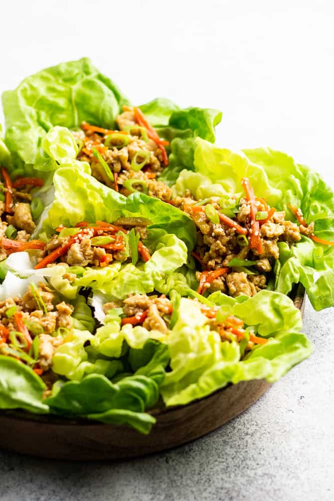 A close up photo of chicken lettuce wraps on a wooden plate.