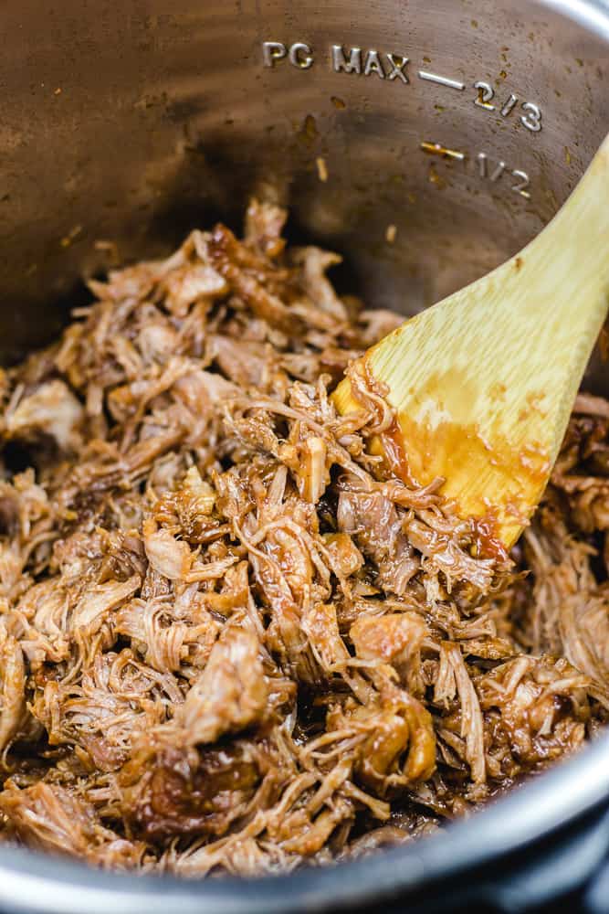 Pulled pork with a wooden spoon in instant pot.