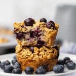 Two Blueberry Baked Oatmeal Cups on a plate with fresh blueberries.