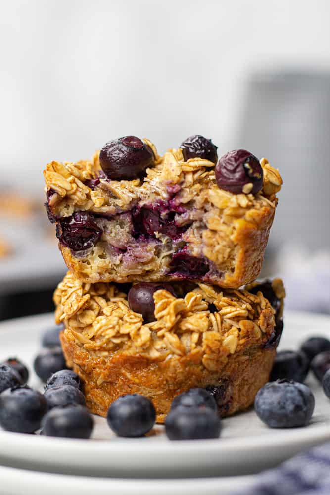 Two Blueberry Baked Oatmeal Cups on a plate with fresh blueberries.