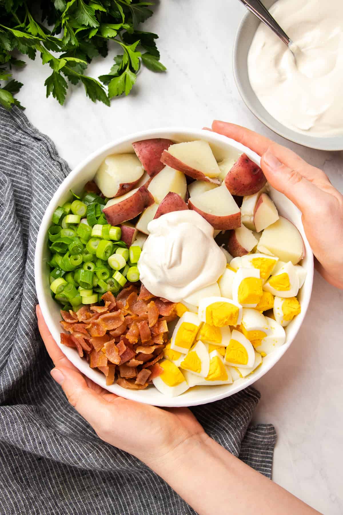 diced Red potatoes, eggs, bacon, green onion, and dressing in a white bowl.