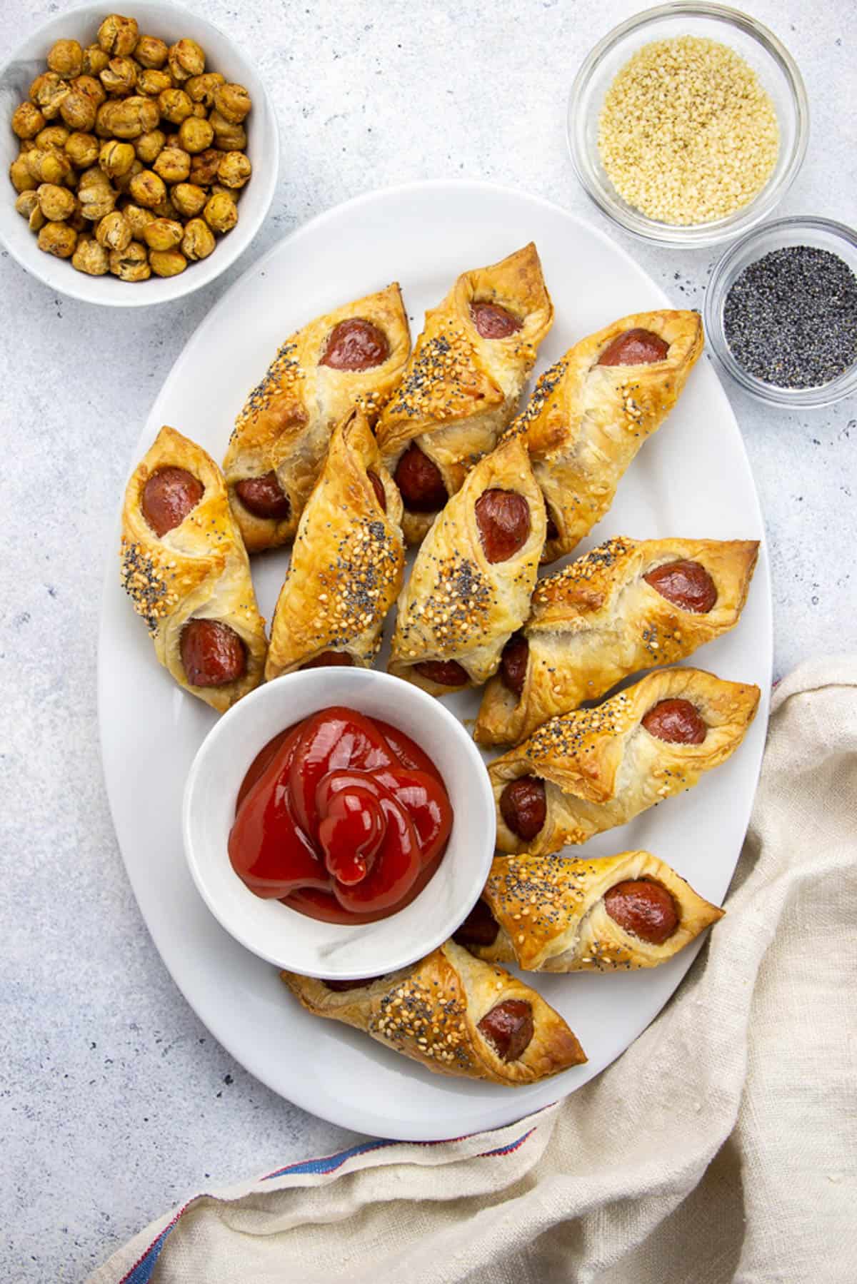 Pigs in a blanbet, served with ketchup on a white oval plate.