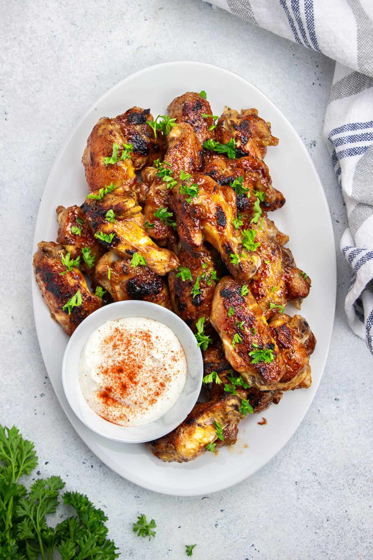 BBQ CHicken wings, served with ranch dressing on an oval white plate.