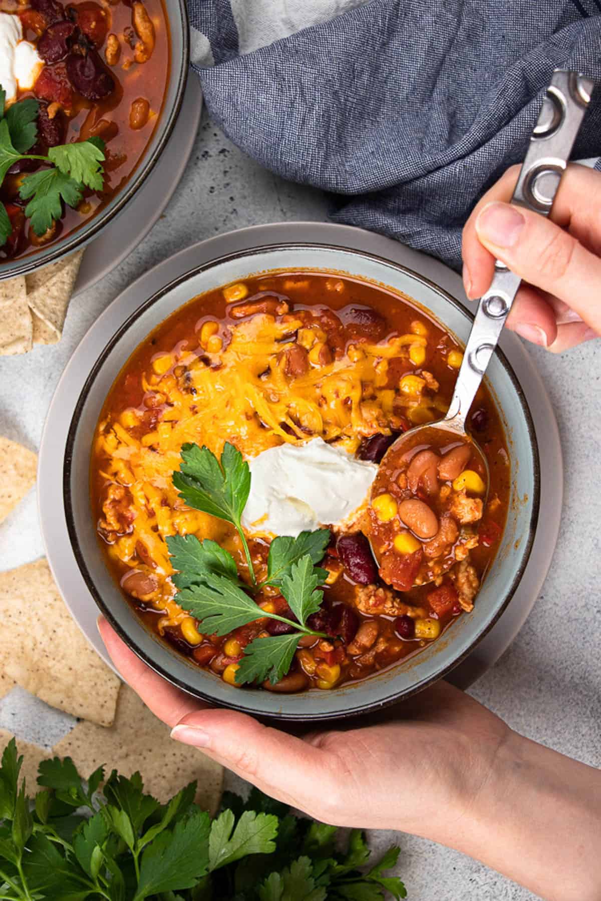 Turkey Chili, topped with sour cream, cheddar cheese, and cilantro in a blue bowl.