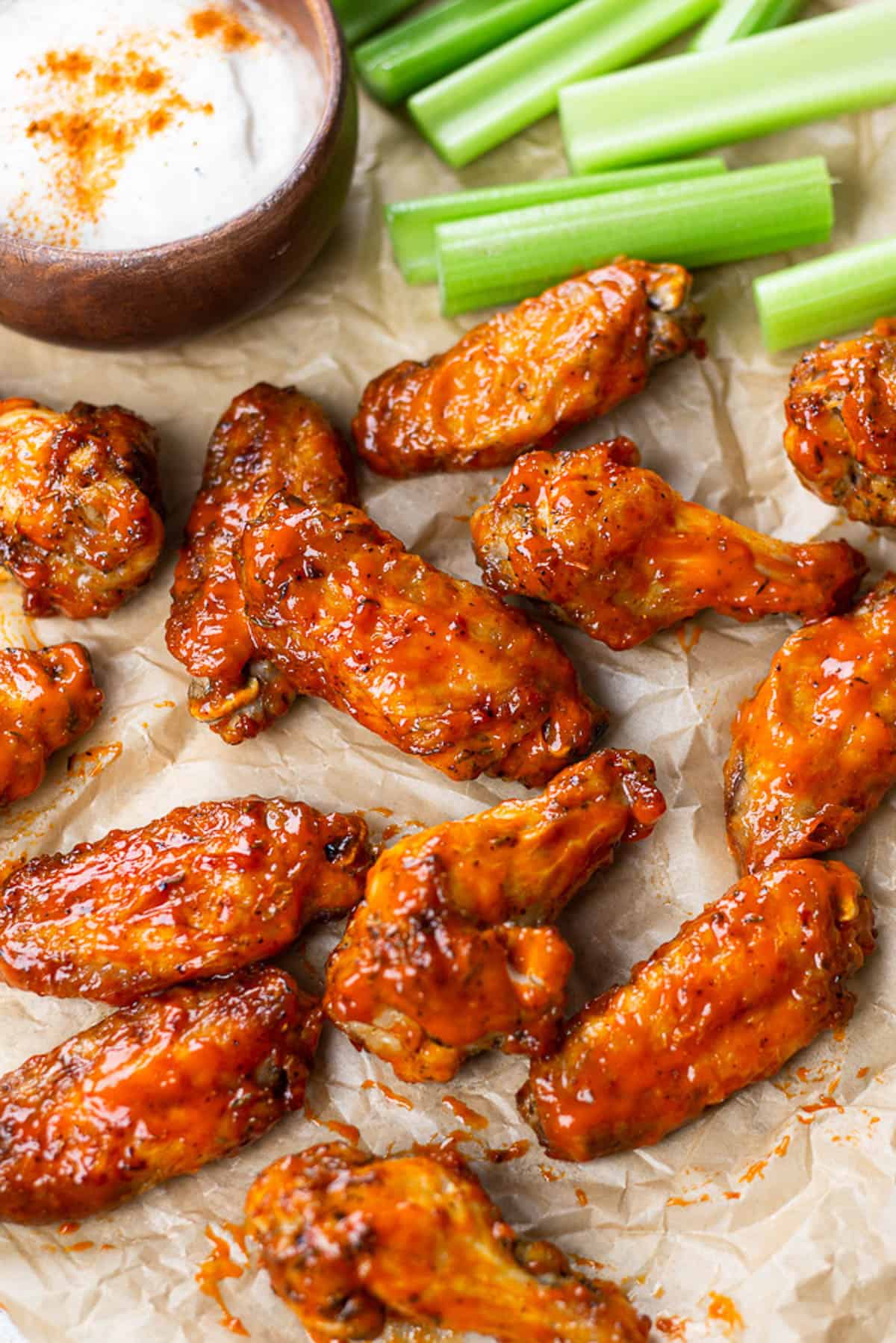 Buffalo wings on a parchment paper with ranch sauce and celery.