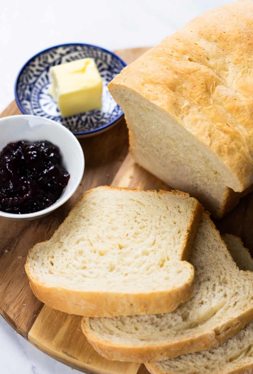 Sliced white bread on a board with butter and jam.