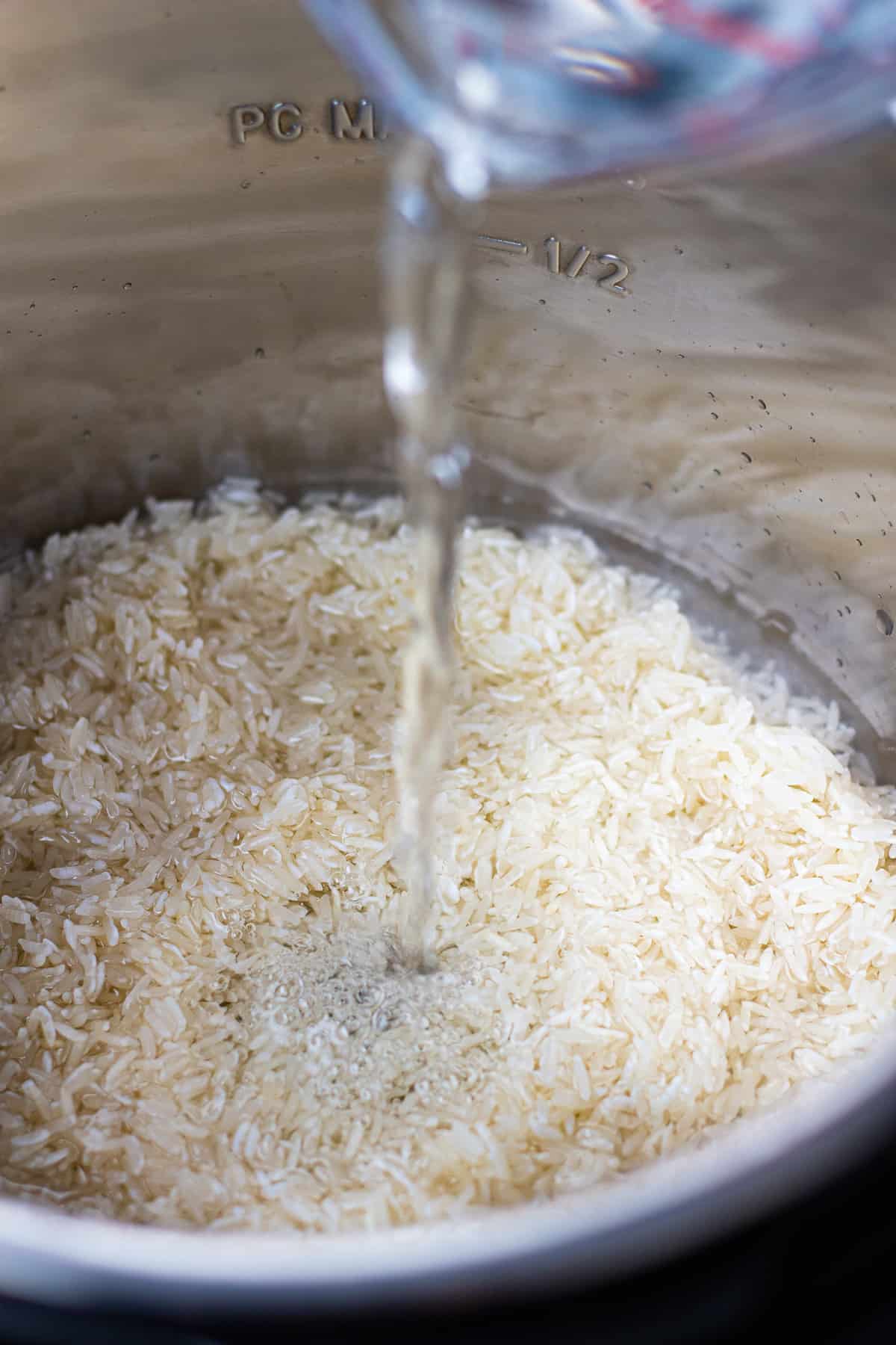 Pouring water in instant pot with uncooked rice.