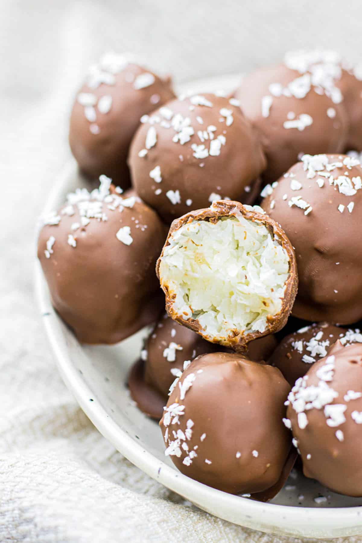 Chocolate covered coconut balls on a white plate.