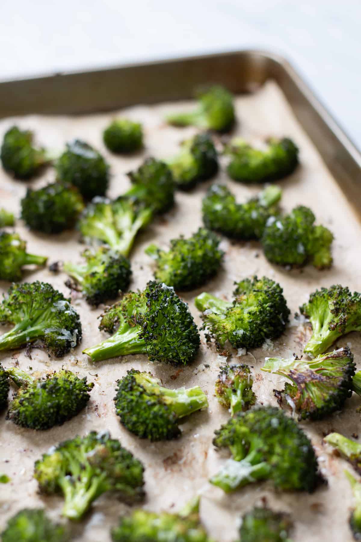 Roasted broccoli on a baking sheet topped with parmesan.