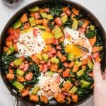 Breakfast hash in a skillet with veggies and eggs.