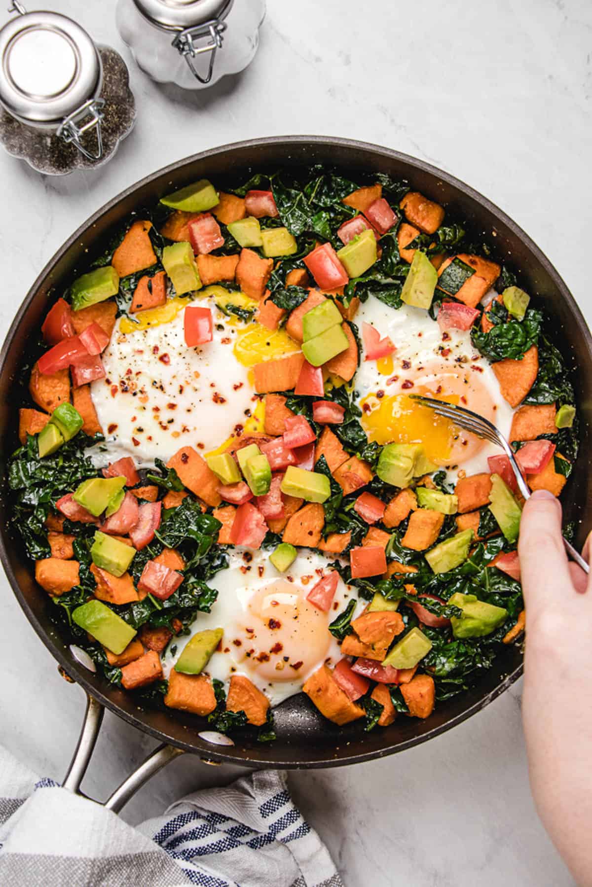 Breakfast hash in a skillet with veggies and eggs.