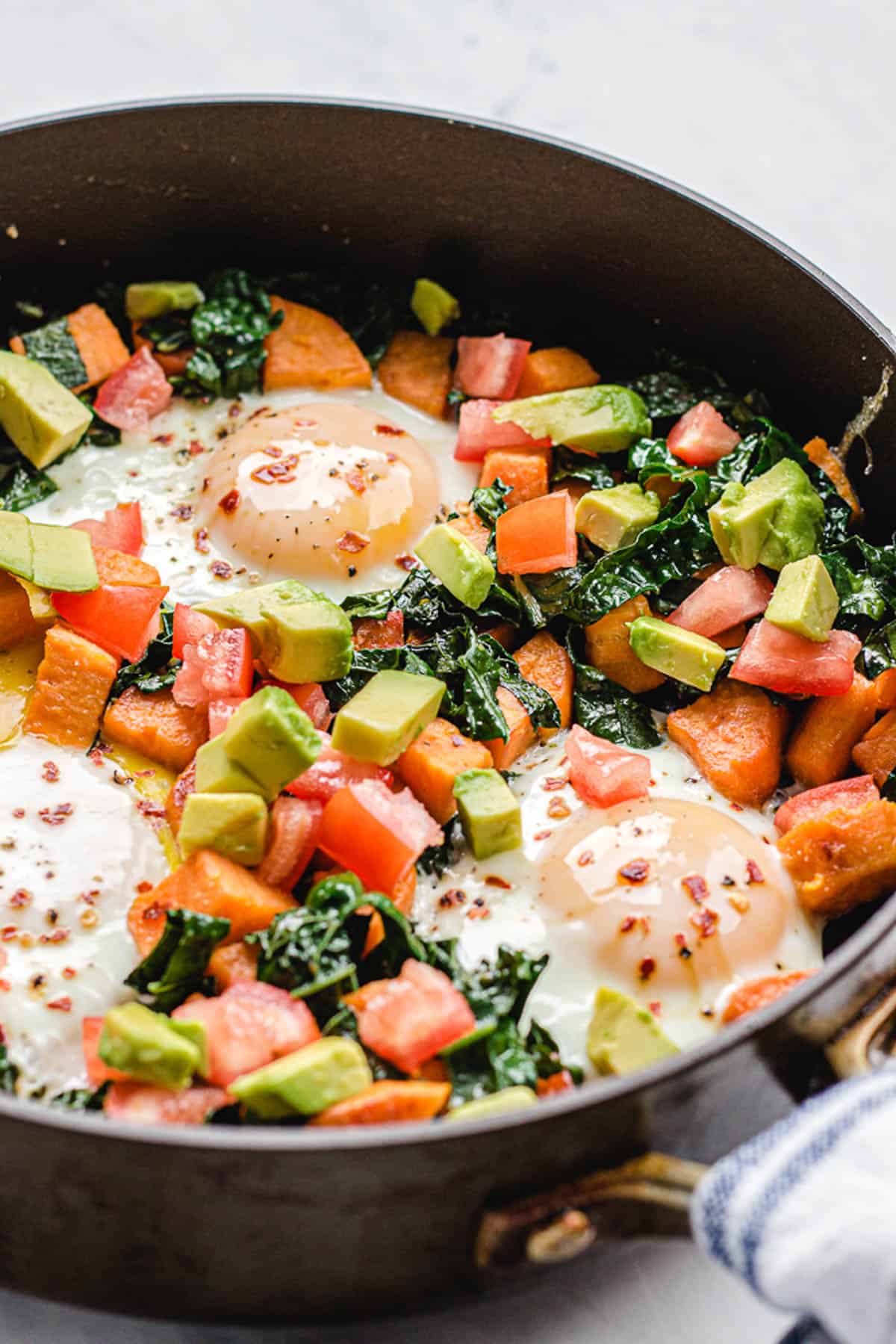 Breakfast hash in a skillet with veggies and eggs.