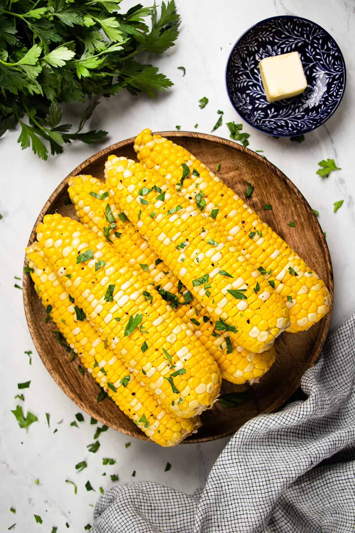 Roasted corn, topped with chopped parsley, on a wooden plate.