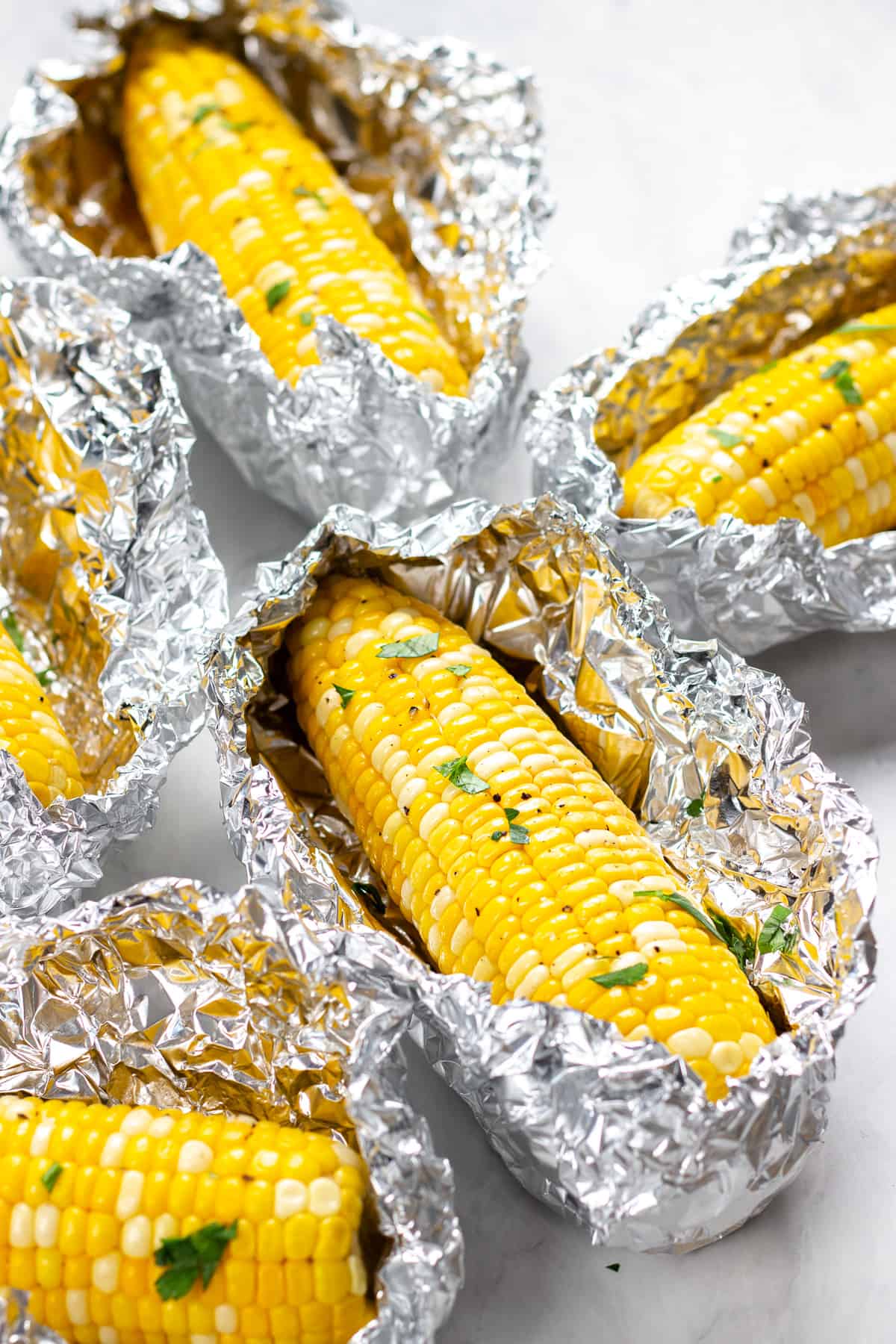 Roasted corn wrapped in foil and sprinkled with parsley.