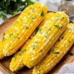 Roasted corn, topped with chopped parsley, on a wooden plate.