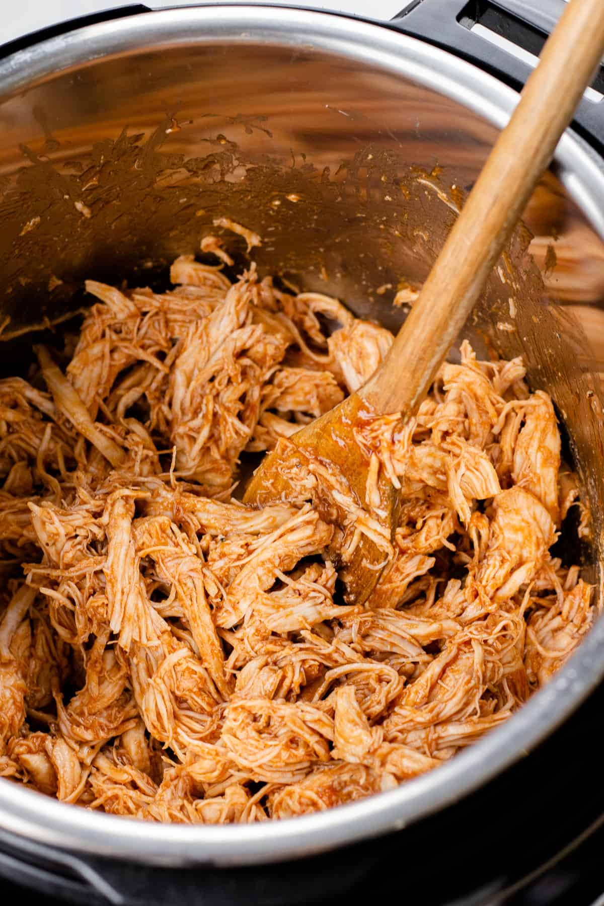 Pulled chicken in instant pot, with a wooden spoon.