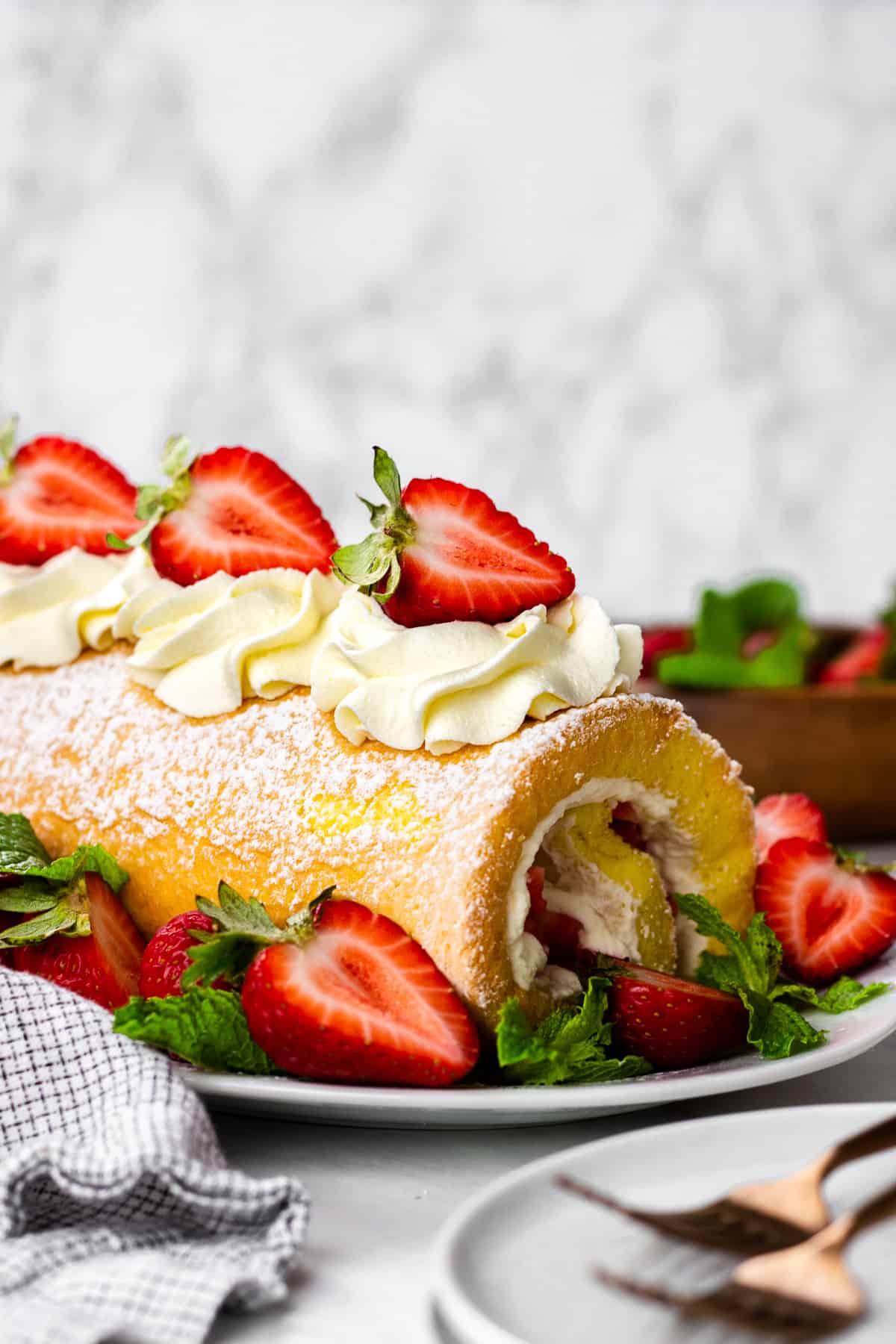 Strawberry Cake Roll decorated with whipped cream and fresh strawberries on a white oval plate.