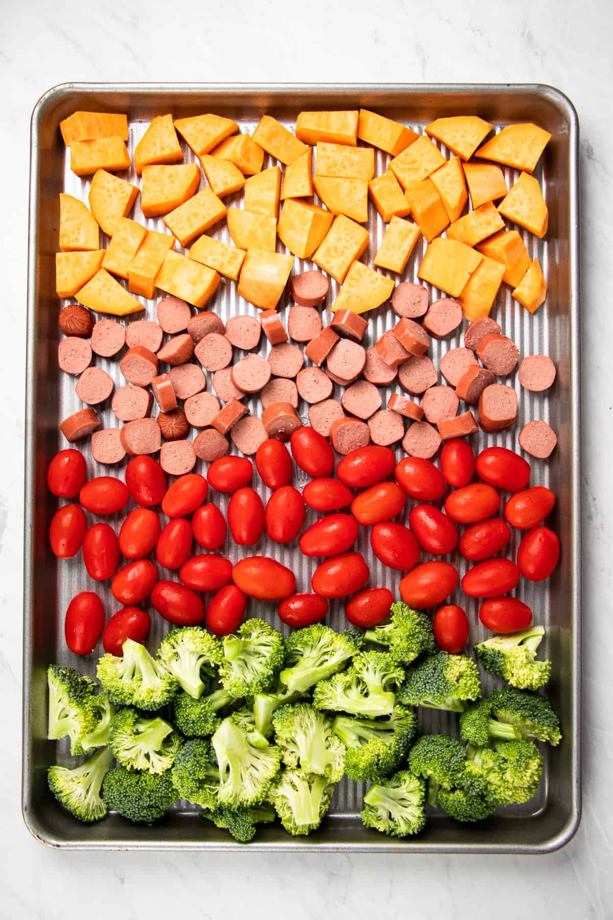 chopped sweet potato, sausage, cherry tomatoes, and broccoli on a sheet pan.