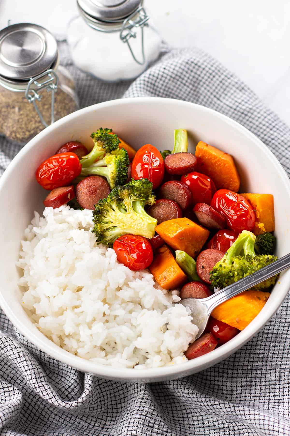 Roasted vegetables and sausage with white rice in a white bowl.