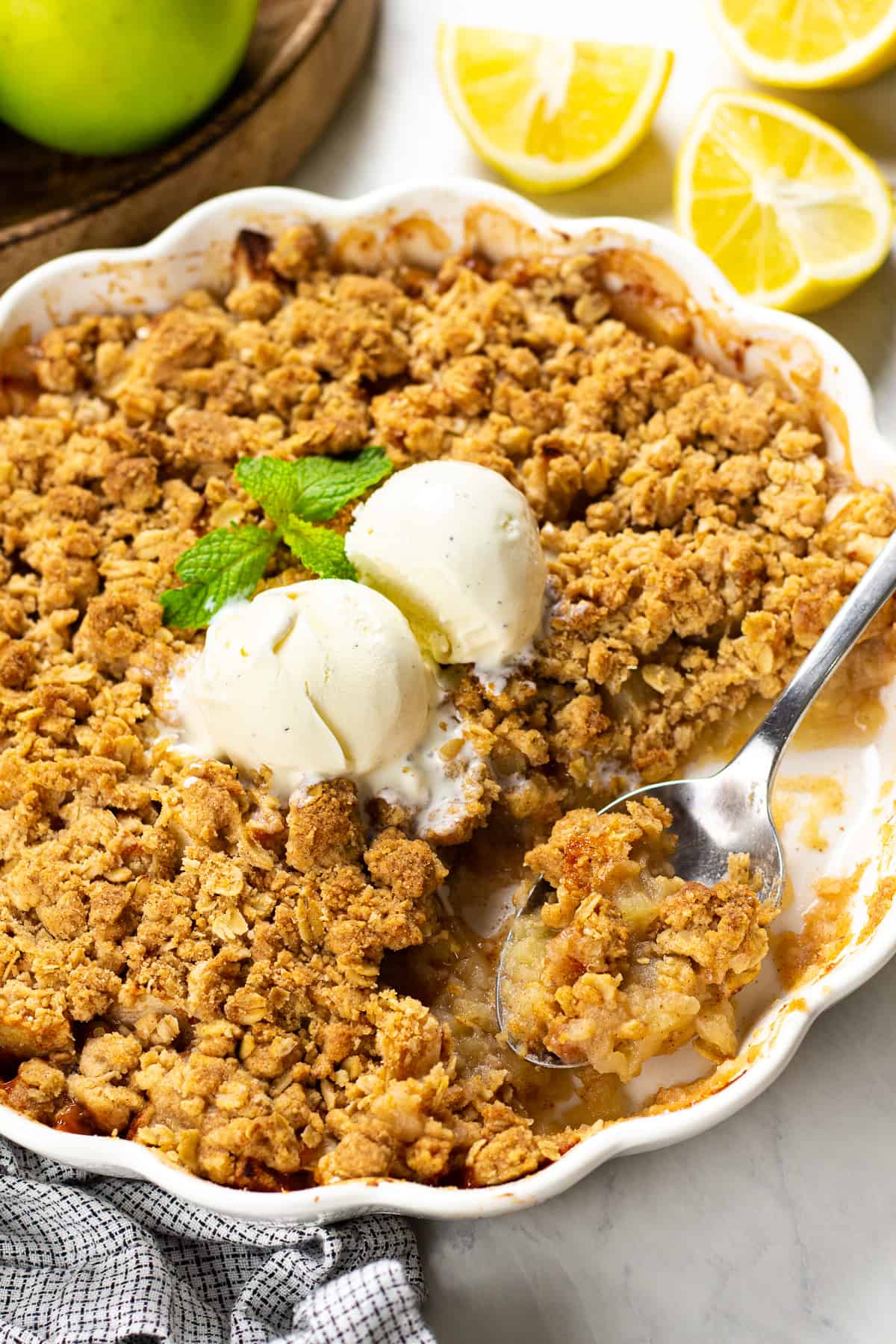 Apple crisp in a white baking pan with a scoop of ice cream on top.