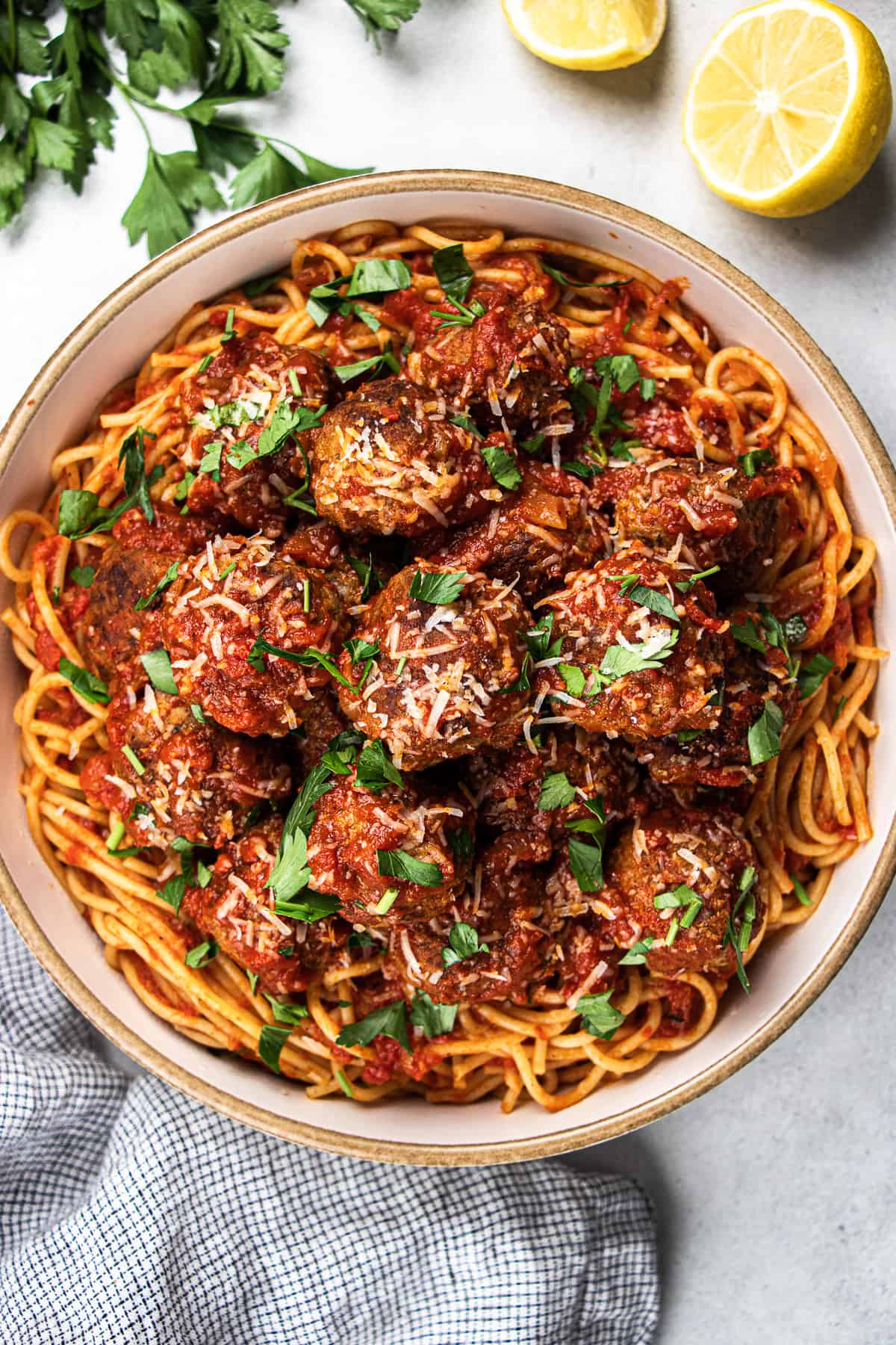 Spaghetti with meatballs, topped with parmesan and chopped parsley, in a large bowl.