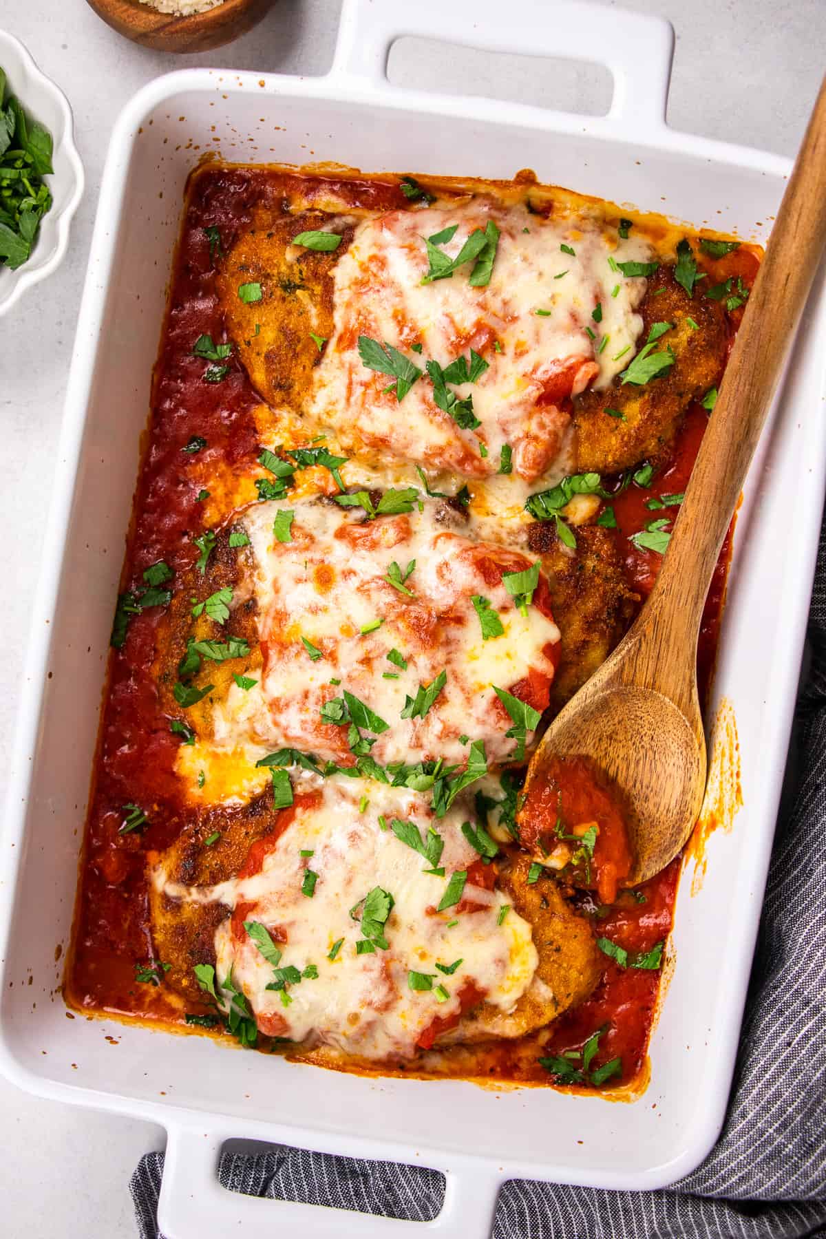 Chicken Parmesan with marinara sauce in a white baking pan.