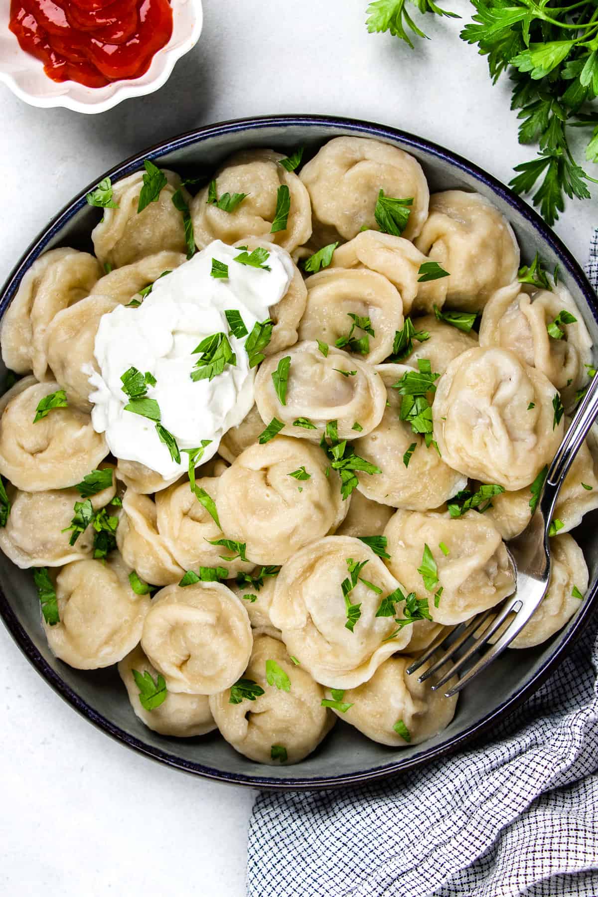 Pelmeni, topped with dill and sour cream, in a dark blue bowl.