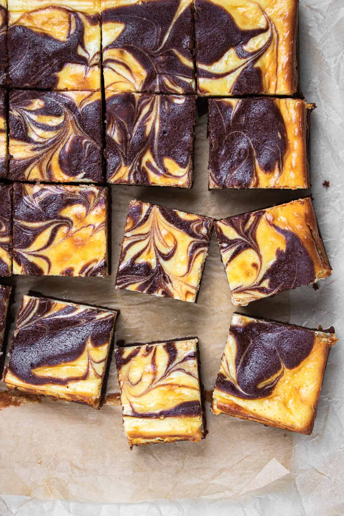 Cheesecake brownies, cut in small squares, laying on a parchment paper.