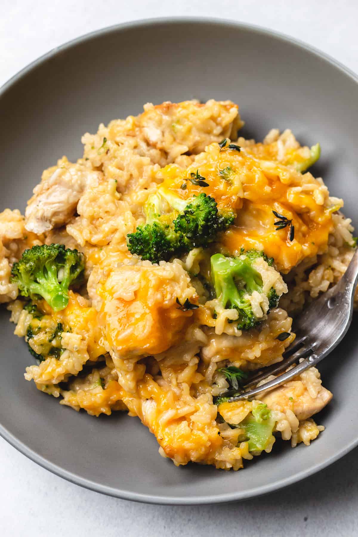 Chicken and rice with broccoli and melted cheese in a grey bowl.
