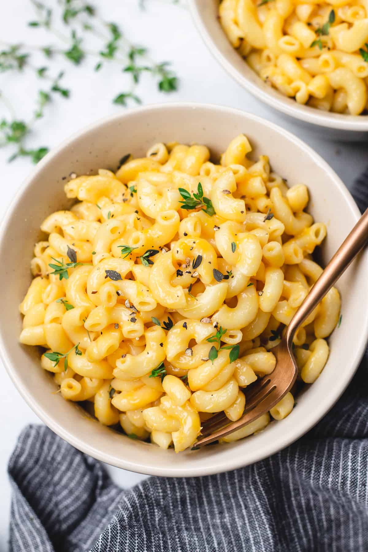 Mac and Cheese  topped with thyme and black pepper in a bowl with a fork.