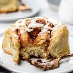 Cinnamon roll topped with icing on a plate with a fork.