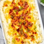 Mashed potatoes topped with cheese and bacon in a white casserole.