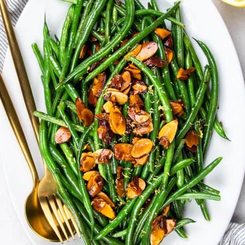 Green beans amandine topped with toasted alonds on a white oval plate.