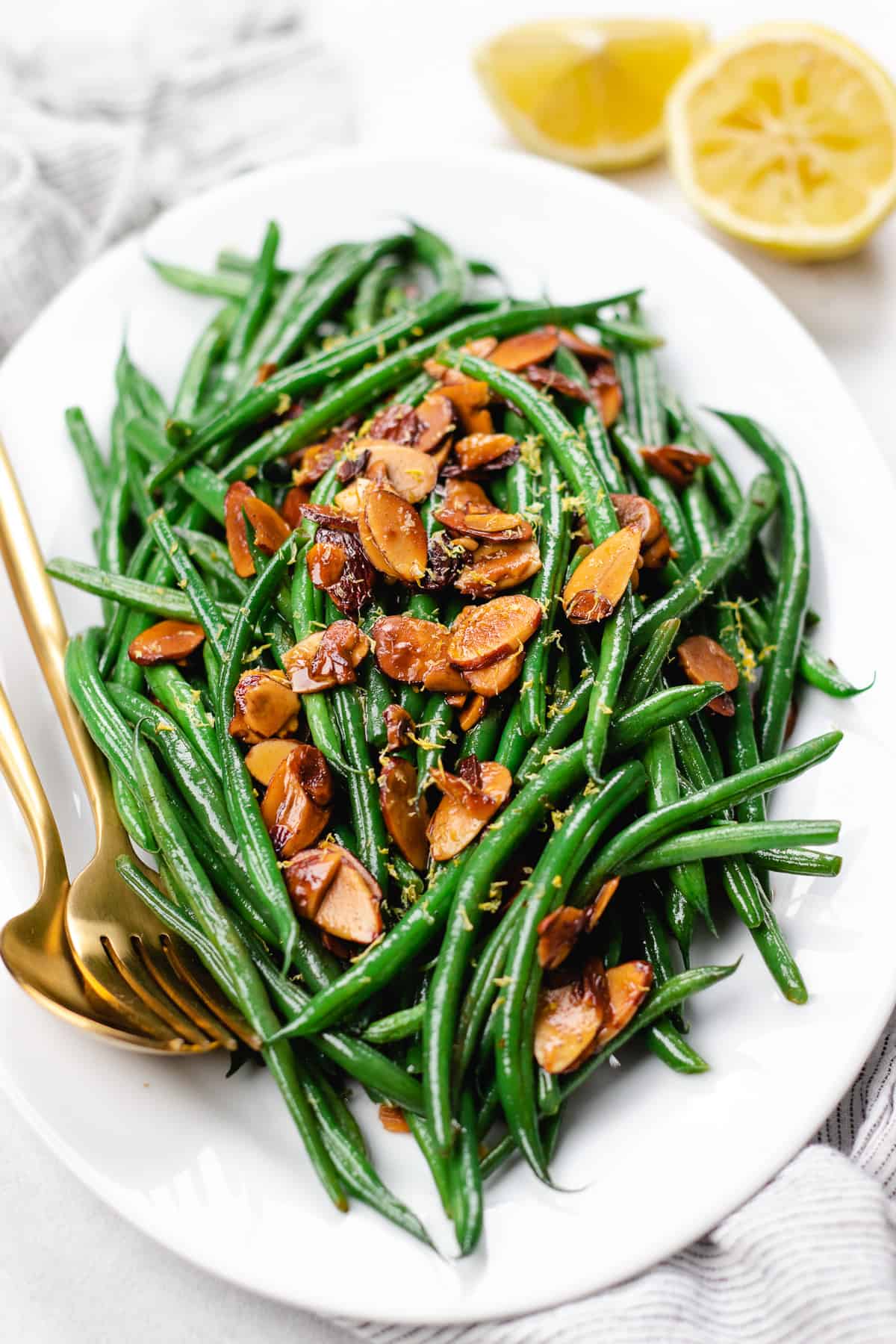 Green beans amandine topped with toasted alonds on a white oval plate.