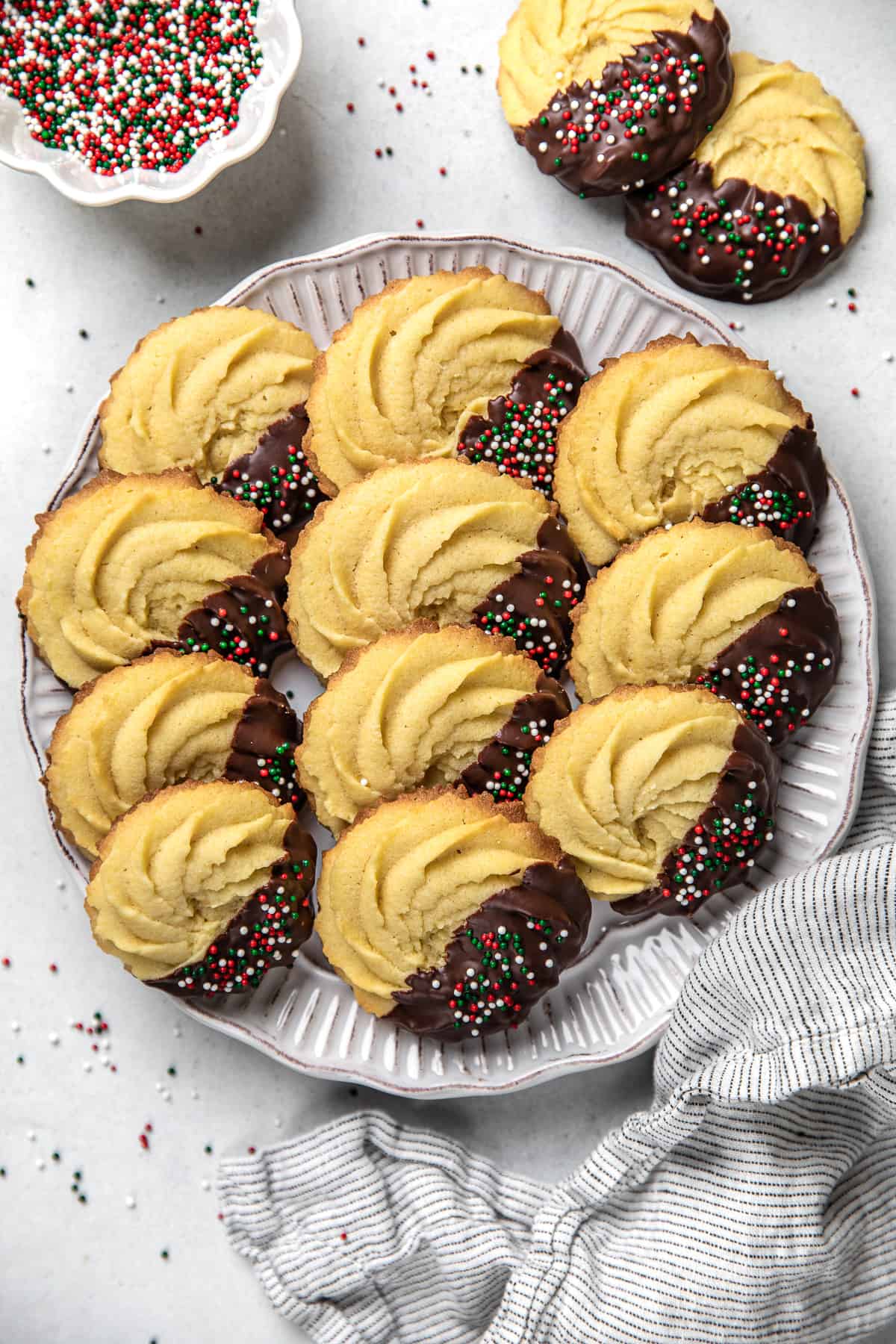 Danish Butter cookies, half covered with chocolate and sprinkles on a white plate.