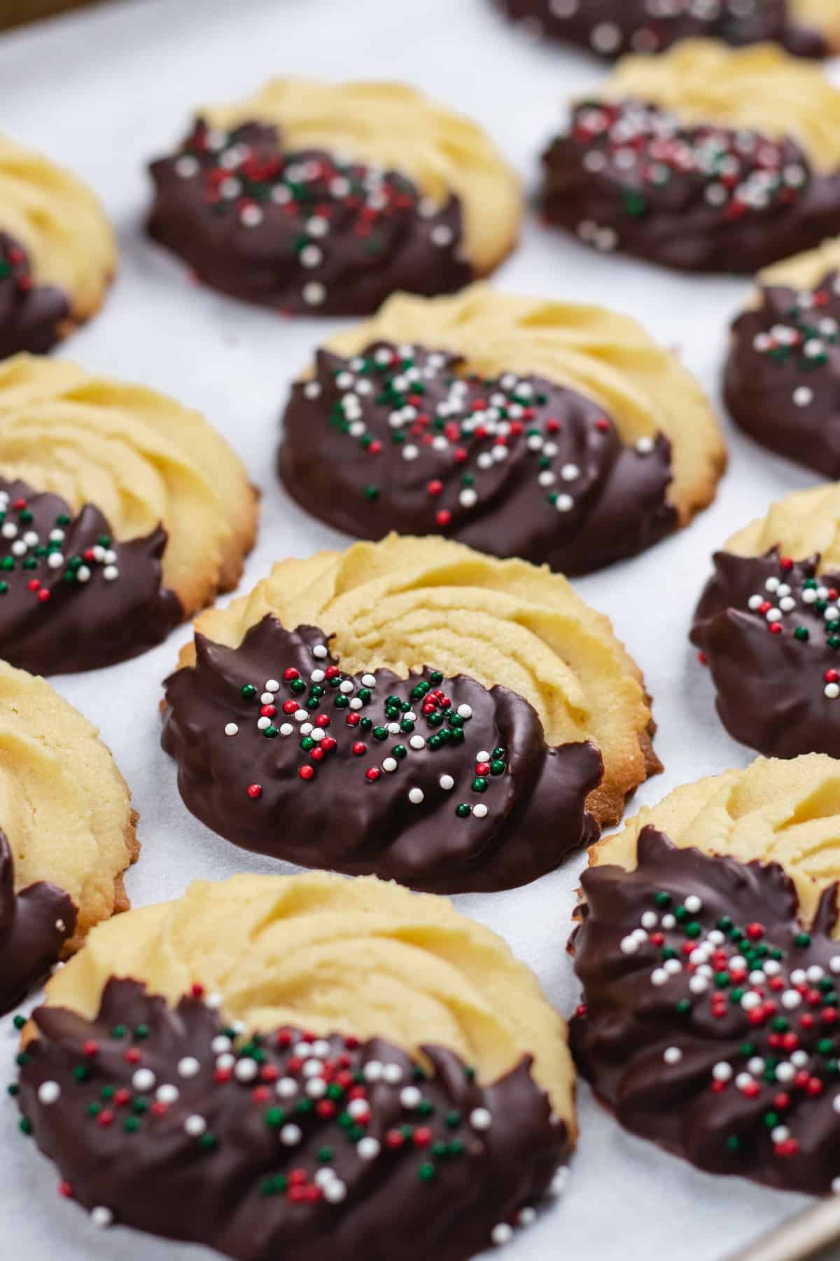 Danish Butter cookies, half covered with chocolate and sprinkles on a table.