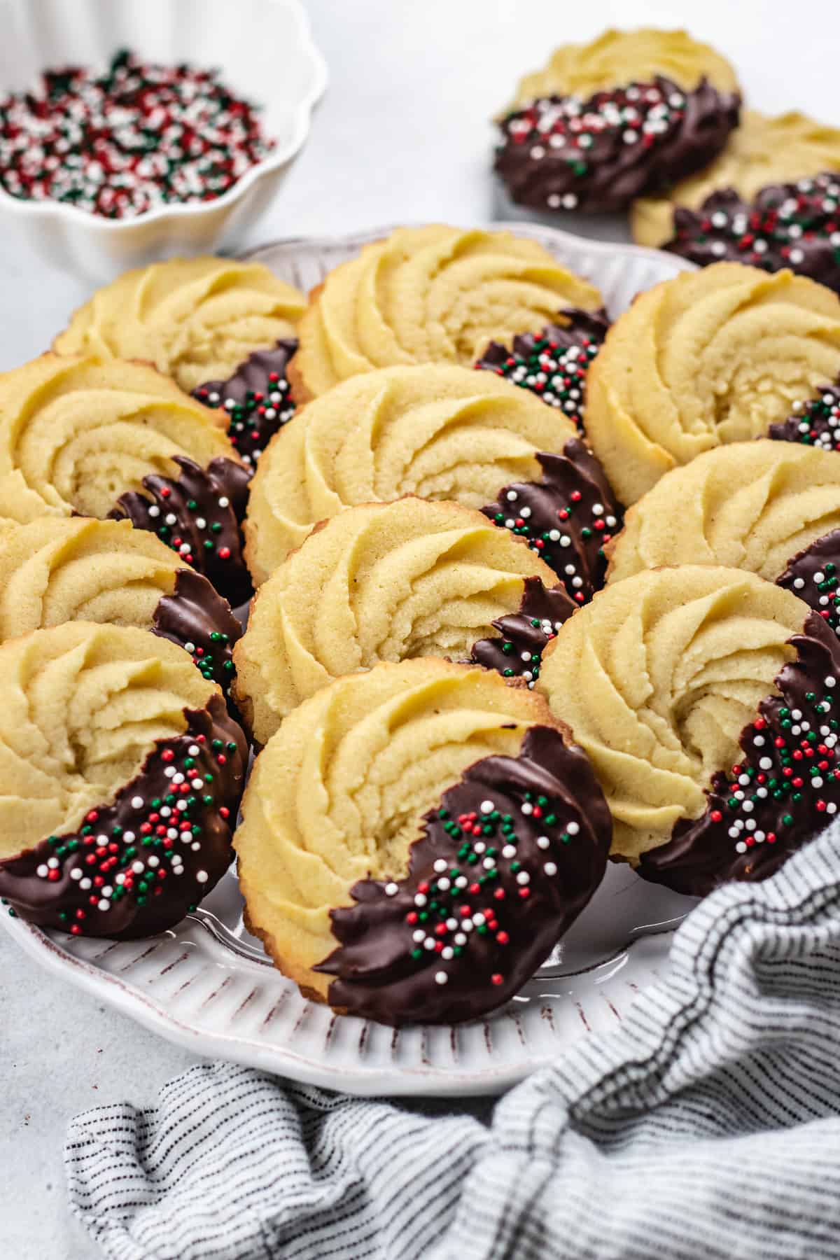Danish Butter cookies, half covered with chocolate and sprinkles on a white plate.