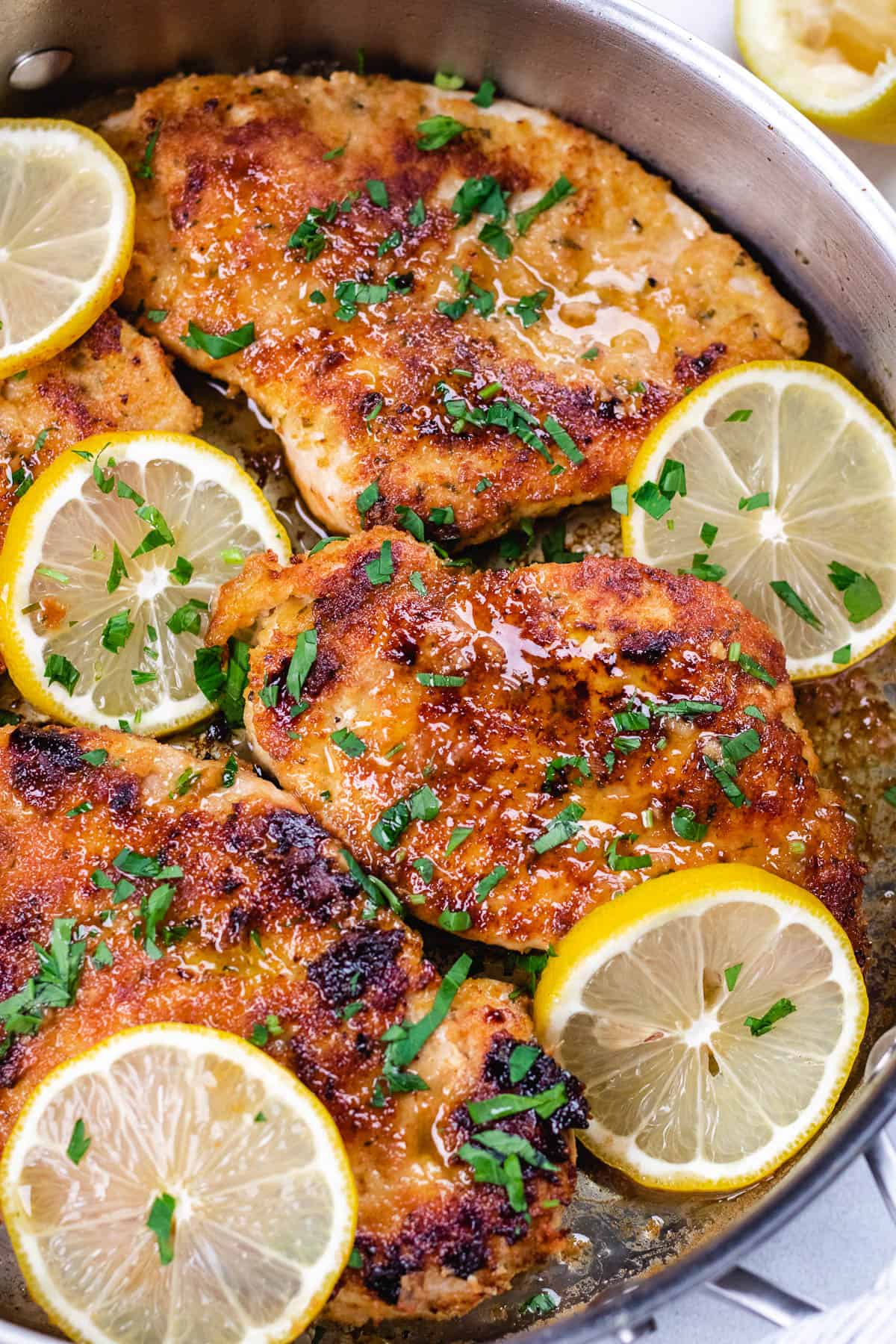 Chicken breasts with lemon sauce in a skillet with lemon slices.