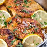 Chicken breasts with lemon sauce in a skillet with lemon slices.