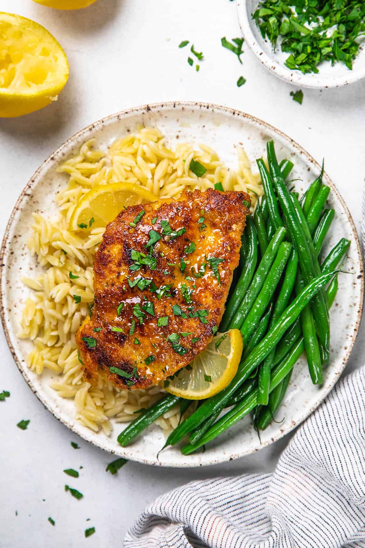 Chicken breast with orzo and green beans on a white plate.