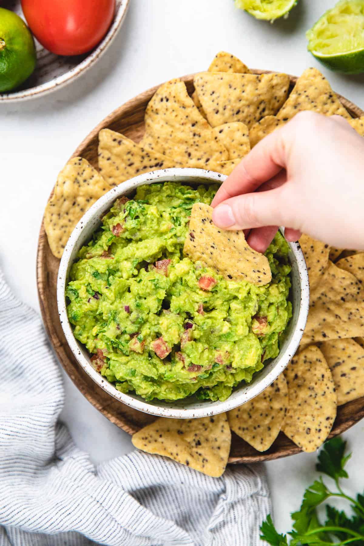 Guacamole in a white bowl with tortillas around it.