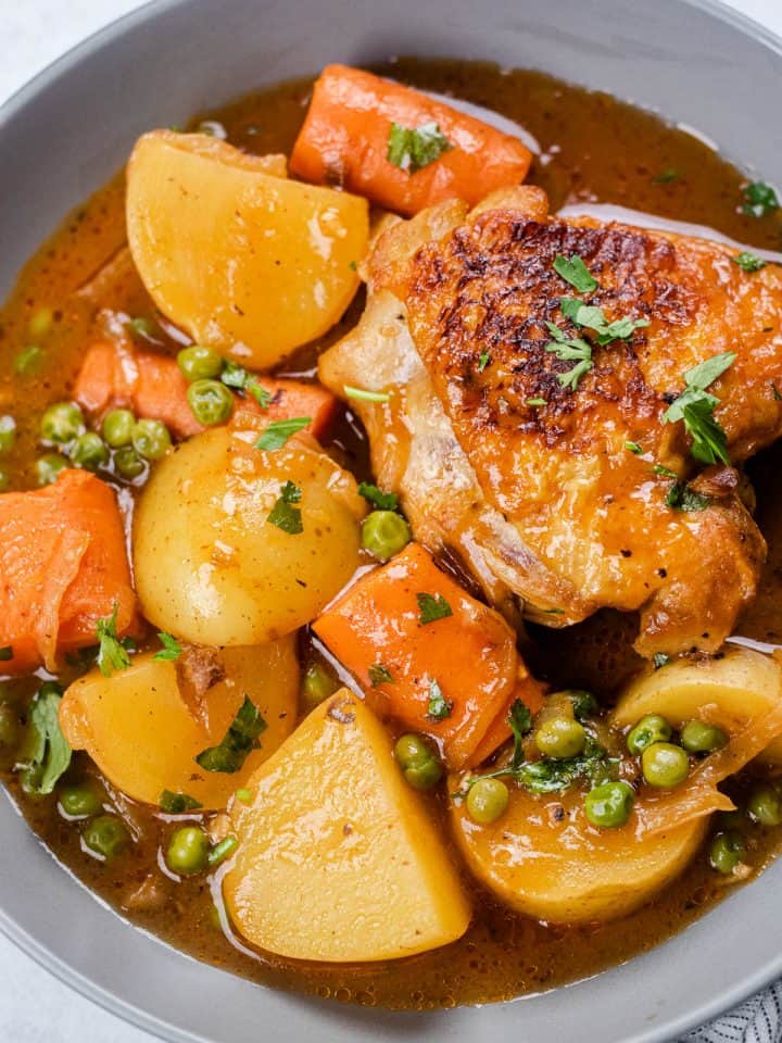 Chicken thigh with potatoes and vegetables in a grey bowl.