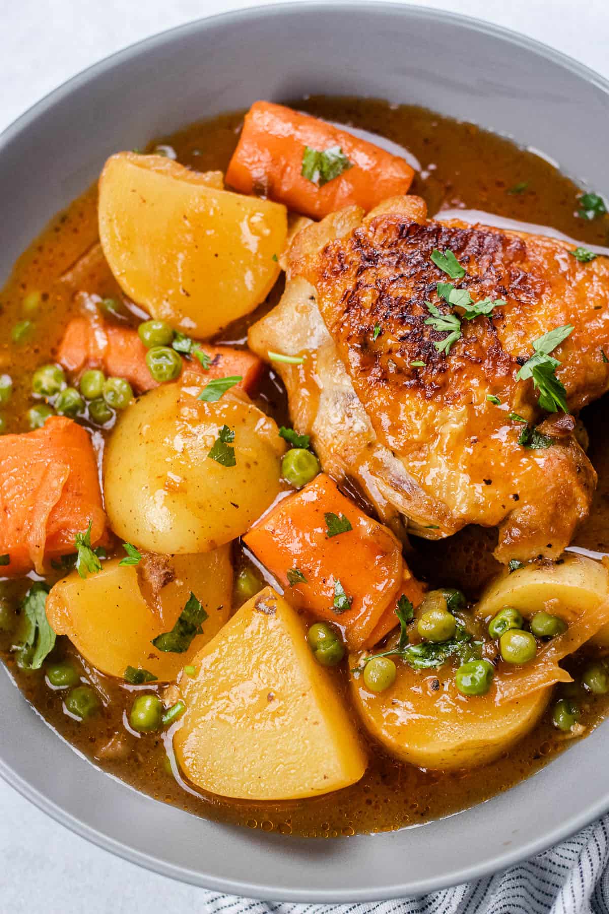 Chicken thigh with potatoes and vegetables in a grey bowl.