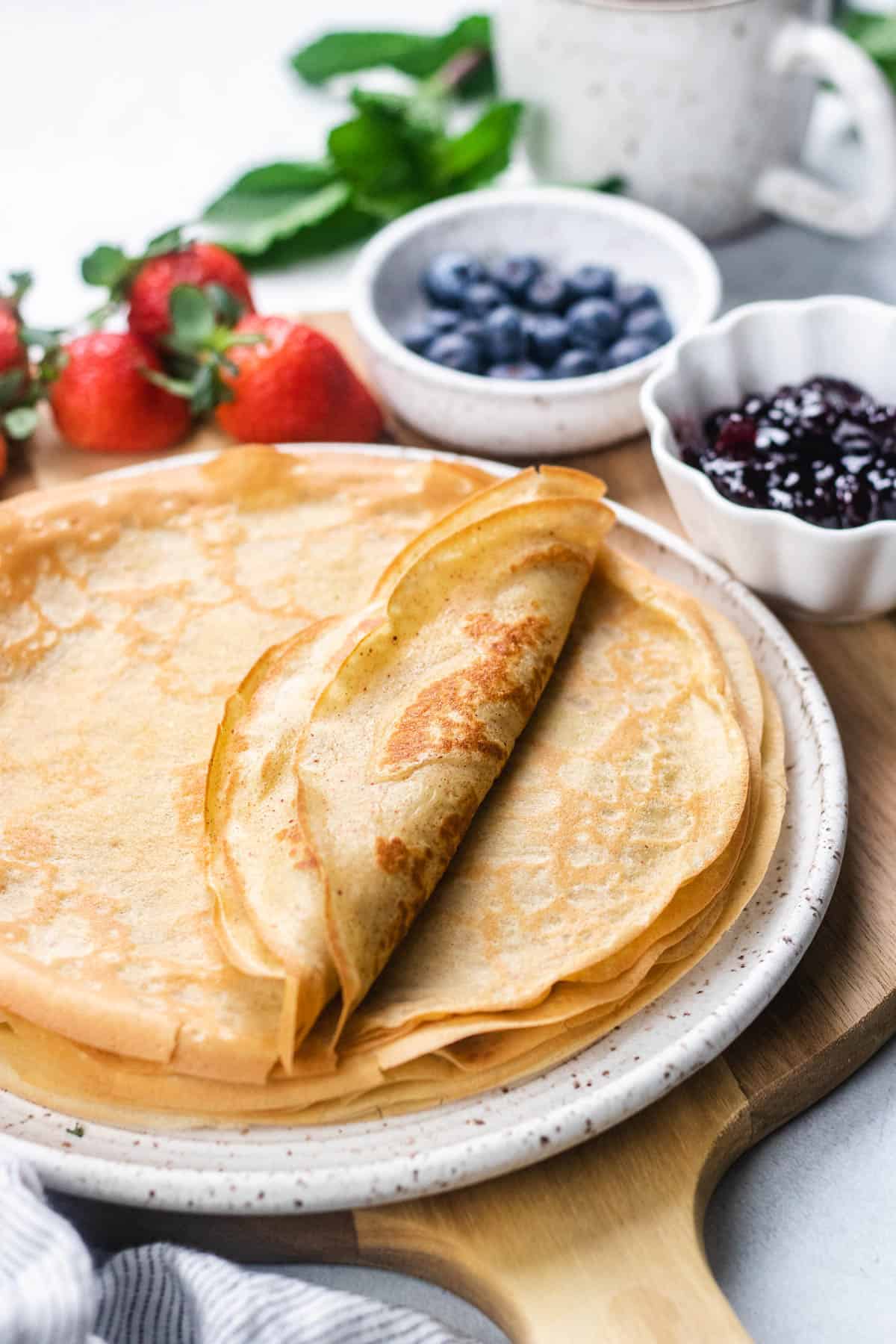 Crepes on a plate with berries and jam.