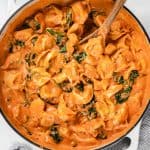 Tortellini in tomato sauce and spinach in a white casserole skillet.
