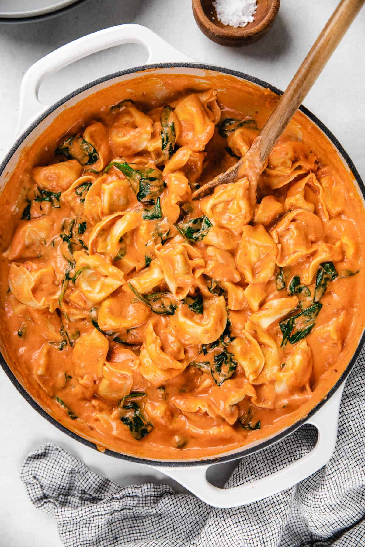 Tortellini in tomato sauce and spinach in a white casserole skillet.
