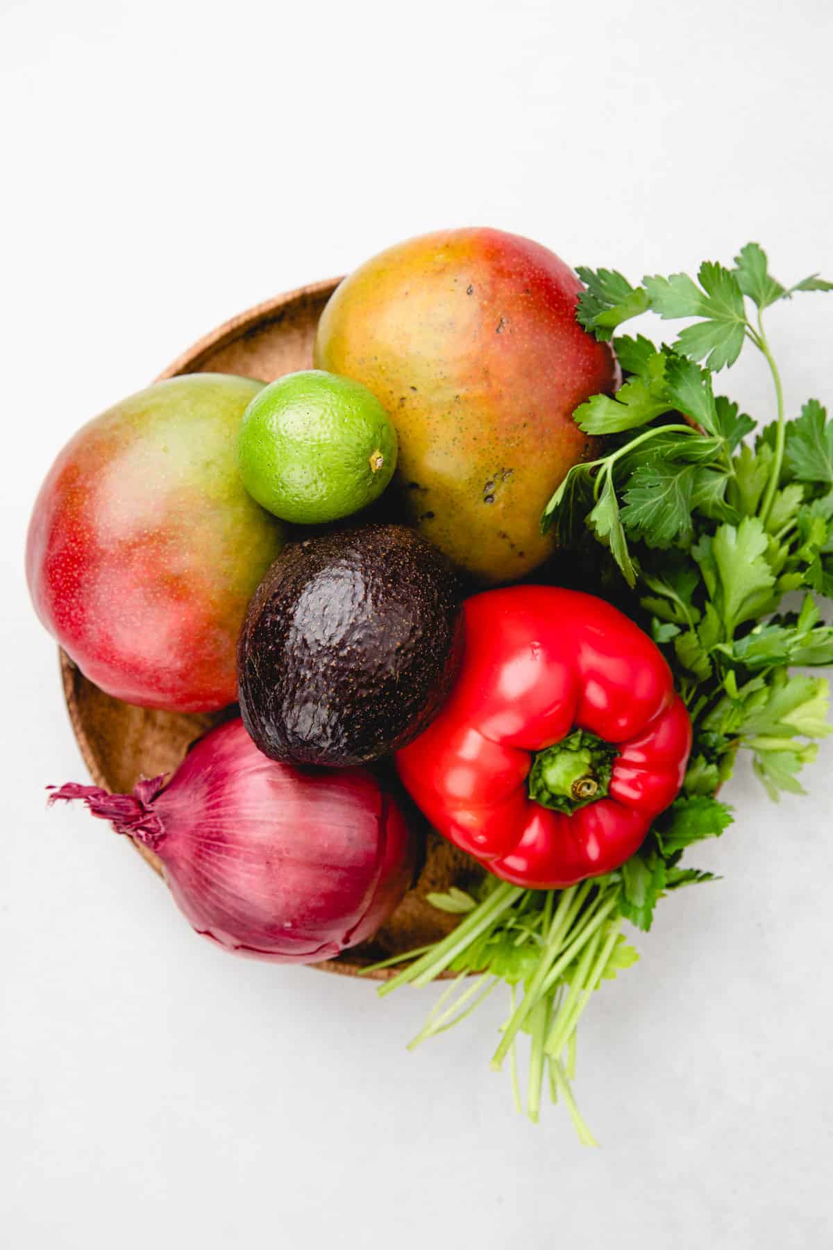 Mango, red onion, avocado, red bell pepper, lime, and cilantro on a wooden plate.